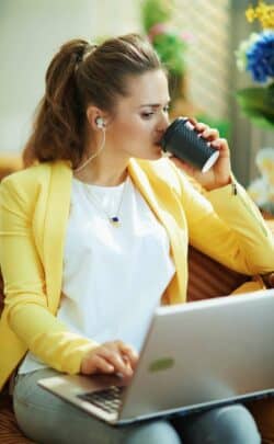 Frau sitzt am Laptop und trinkt Kaffee, während sie Neues lernt